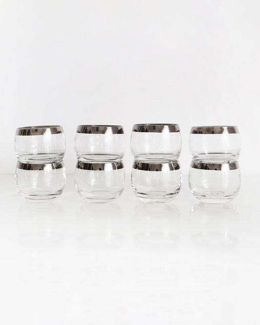 A row of four silver rim roly poly glasses that are stacked in twos on a white table against a white backgroundA row of for silver rim roly poly glasses that are stacked in twos making eight total glasses. The glasses are on a white table against a white background