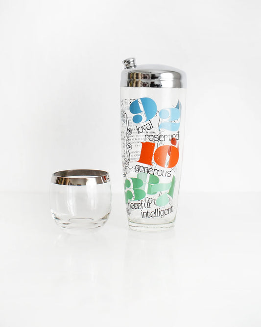 A numerology game with colorful numbers and one word trait explanations underneath with a chrome metal lid with screw on spout. A silver roly poly glass sits next to the shaker.