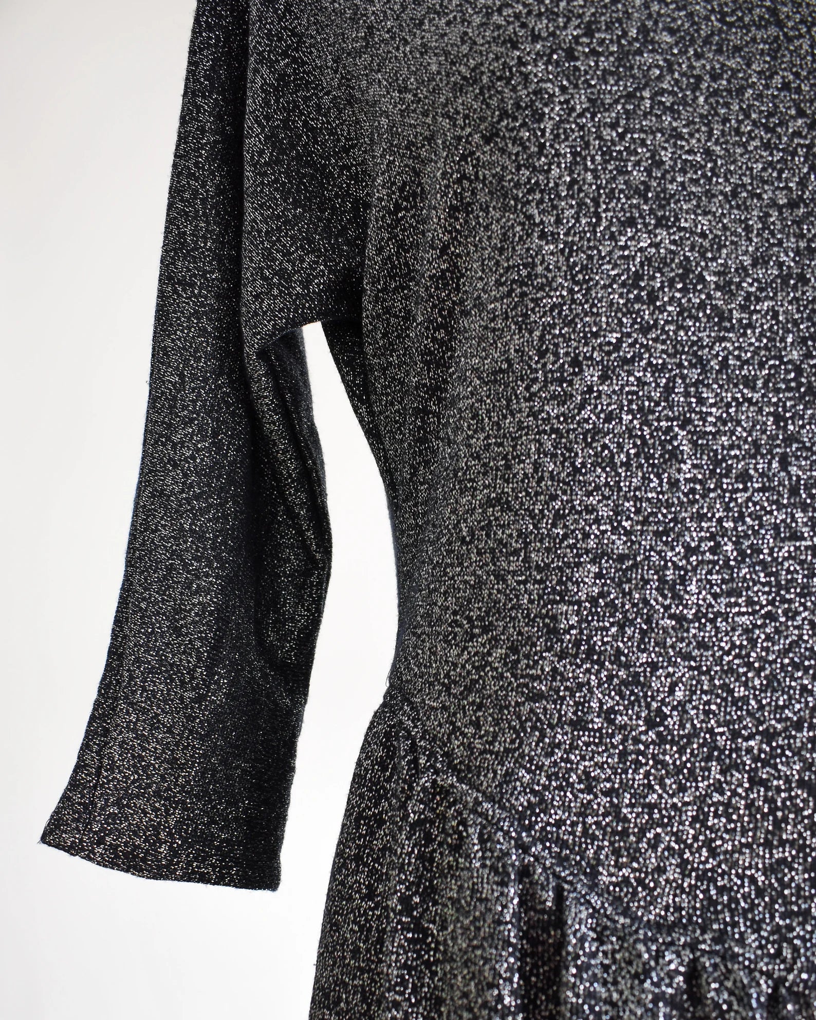 Close up of the black and silver metallic lurex threads that are woven throughout, which gives the garment lots of sparkle. The garment is modeled on a dress form.