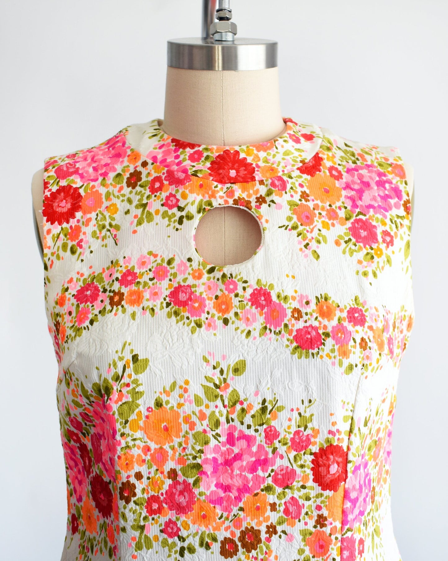 Close up of the vibrant pink, orange, and green floral print and the circle cut out under the collar on the dress. The dress is on a dress form.