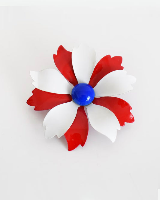 A vintage 60s mod floral brooch that has red and white petals with a blue rounded center.