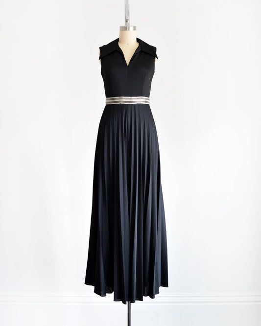 A vintage 70s black jumpsuit with collared neckline, striped waistband, and accordion pleated wide leg pants on a dress form.