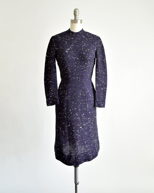 A vintage 50s dress that has black and purple wool with white flecked spots on a dress form.