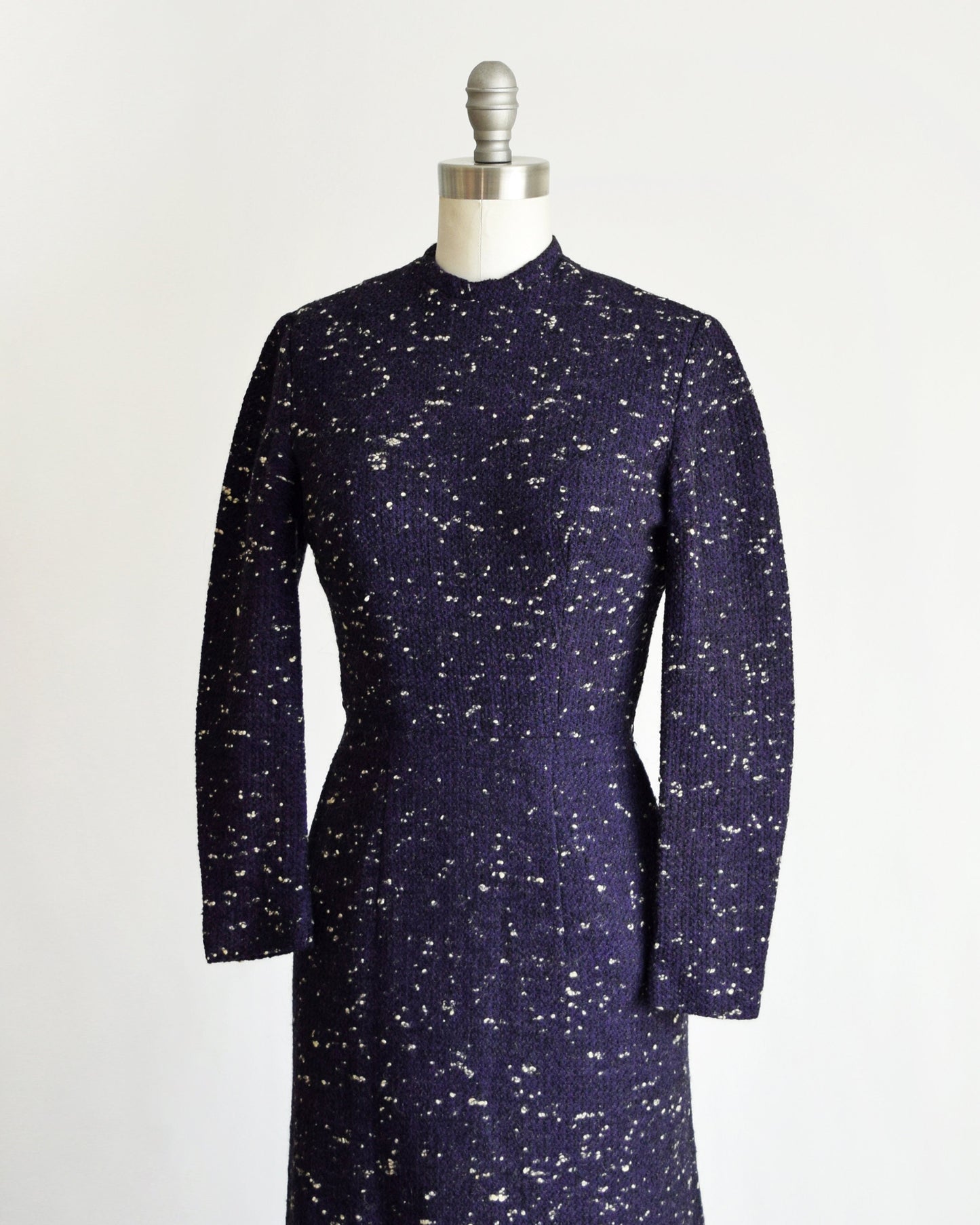 Side front view of a vintage 50s dress that has black and purple wool with white flecked spots on a dress form.