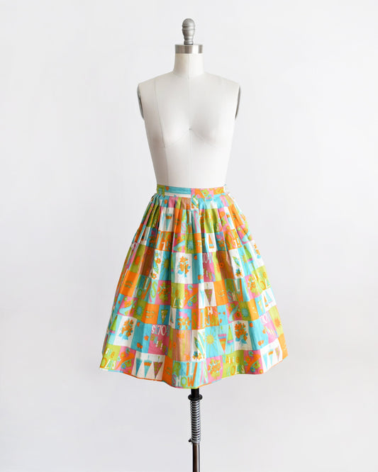 A vintage 50s skirt has an April showers theme with colorful blocks of flowers, umbrellas, shoes, the sun, and the words April Showers and Raining Violets in a classic mid century print. Skirt is modeled on a dress form