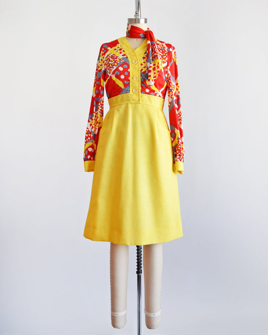 A vintage 70s dress that has a red and yellow multicolor geometric print bodice, a-line style skirt with two front pockets, and matching scarf.