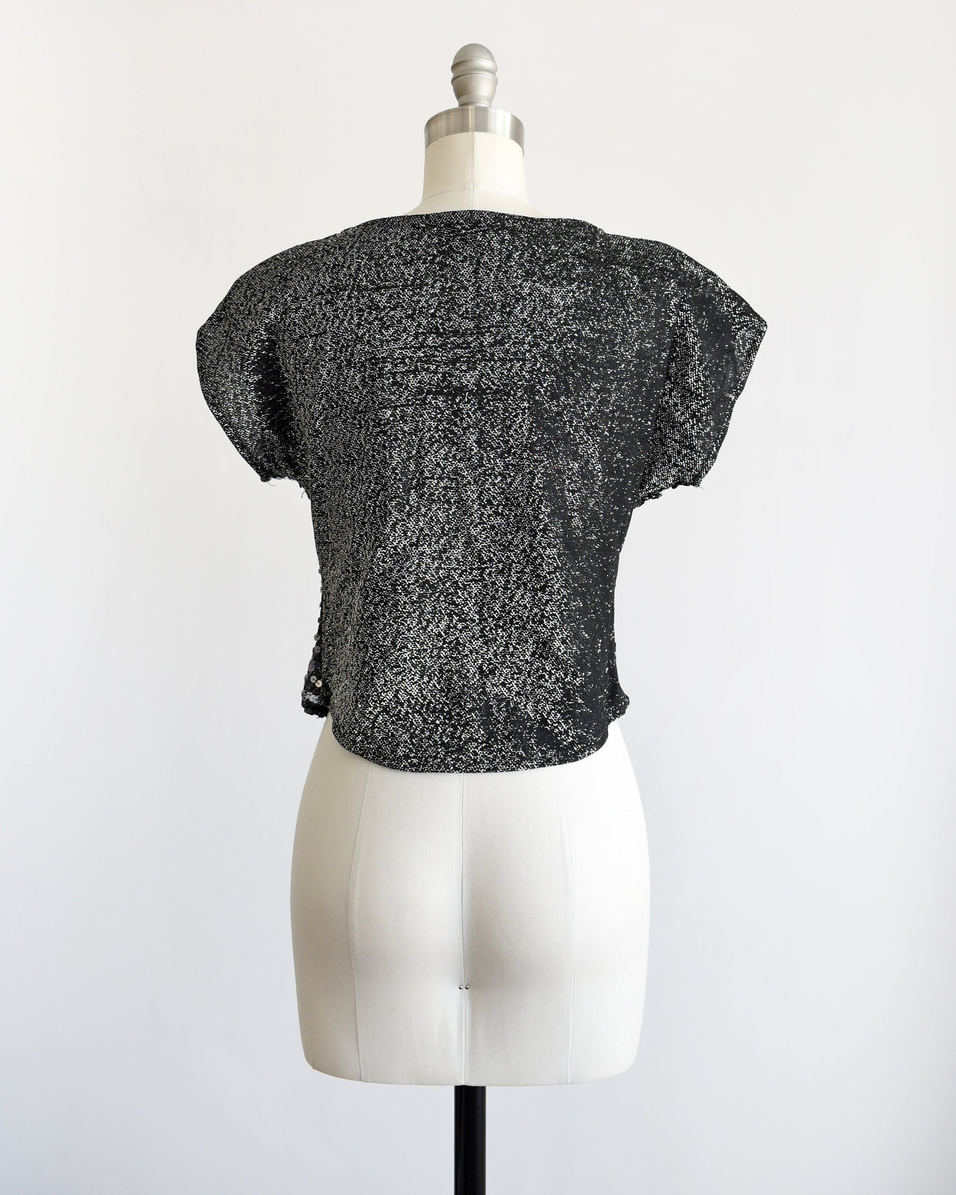 Back view of a  vintage 80s sequin top that   has a black and silver lurex back. Cap sleeves. Rounded waistline. 