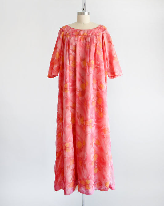 A vintage floral maxi dress with pinks, dark red, orange, and yellow floral print. The dress has half sleeves and is on a dress form.