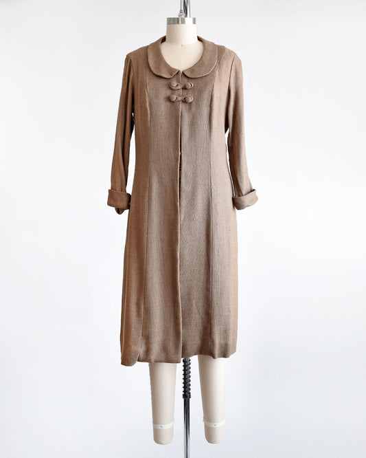 A vintage late 50s early light brown wool swing coat. The coat has a rounded Peter Pan style collar, four buttons underneath and cuffed long sleeves. The coat is modeled on a dress form.