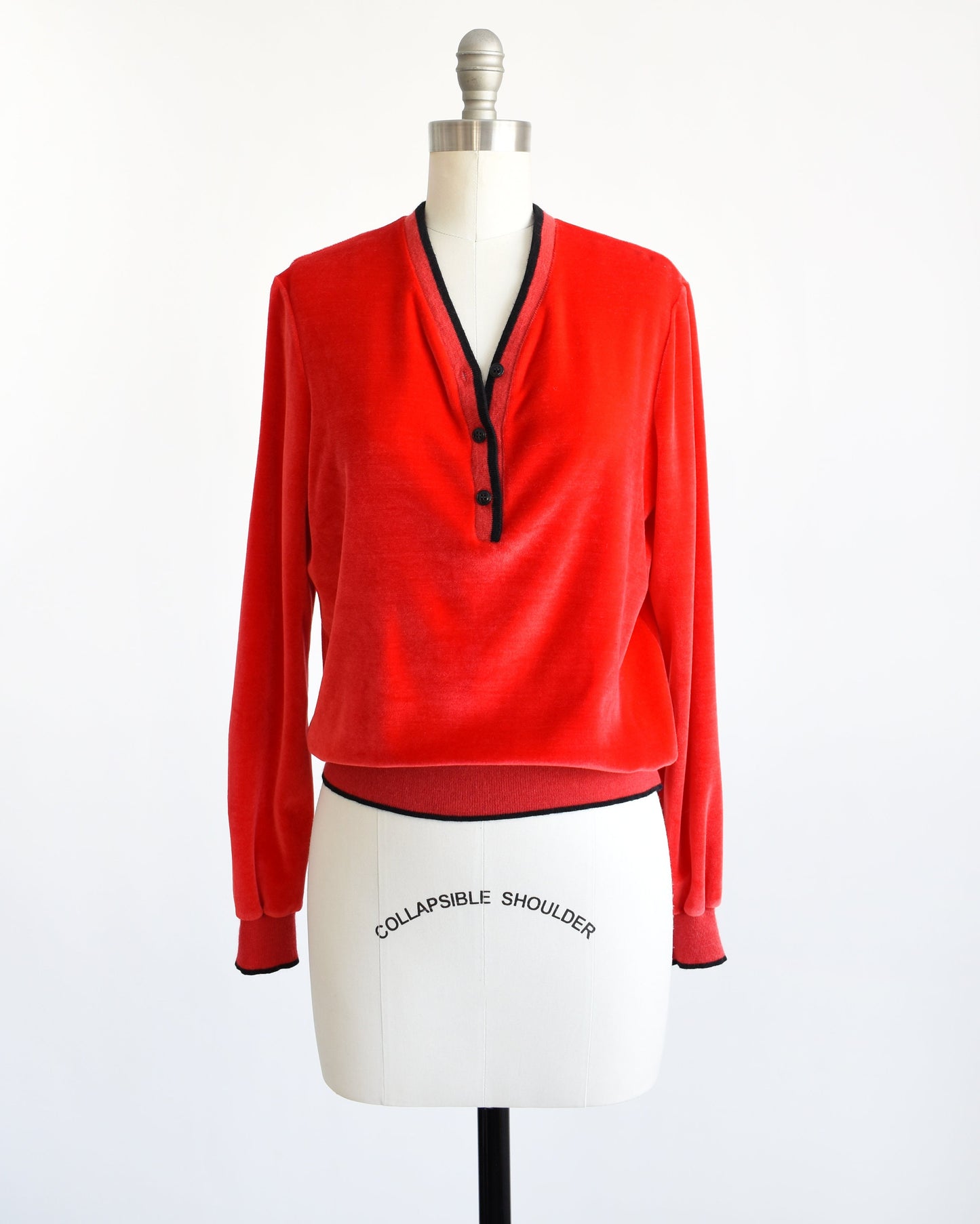 A vintage 70s red velour top with black trim along the v-neckline, cuffs, and hem. There are three black buttons on the front and the top is modeled on a dress form.