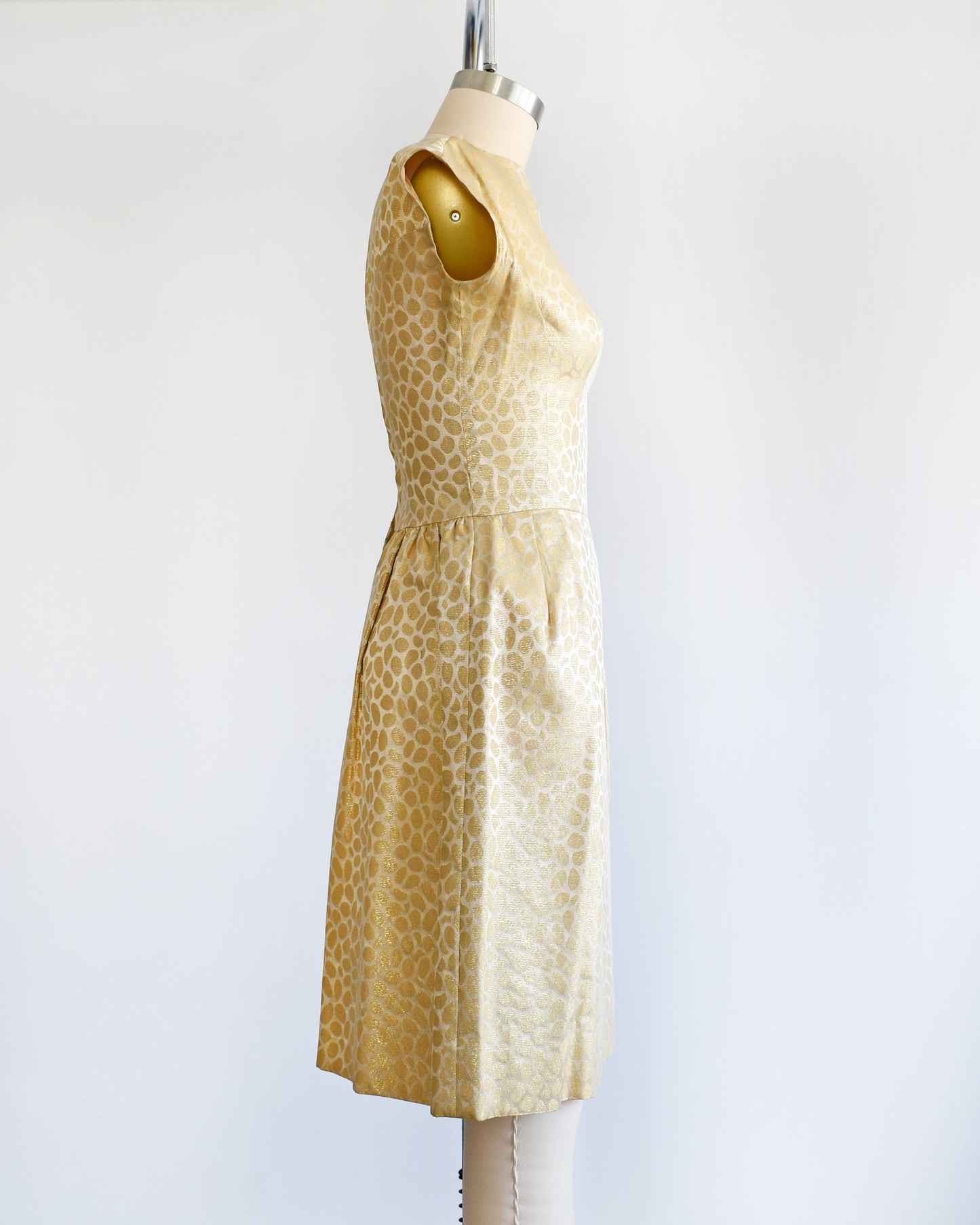 Side view of a vintage 60s gold dress with metallic gold brocade polka dots. The dress is modeled on a dress form.