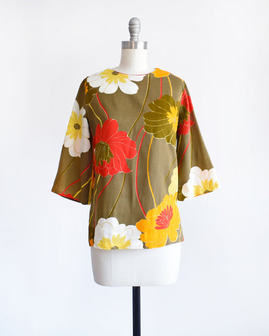 A vintage light brown blouse with a large red, orange, white, and yellow floral print on a dress form.