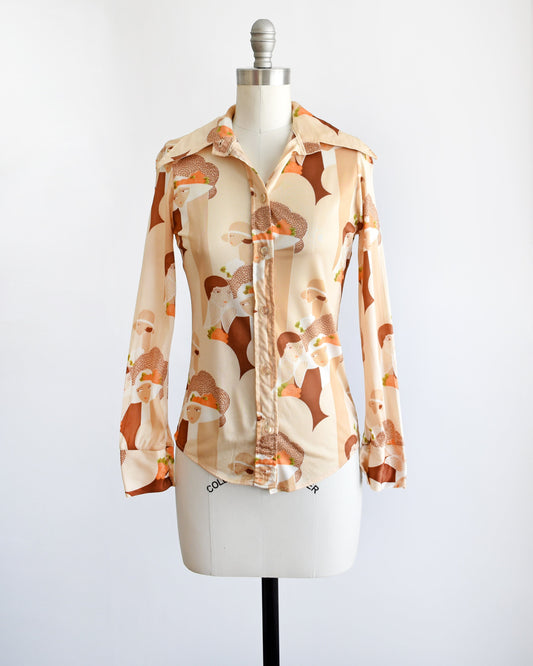 A vintage 70s blouse that has a novelty print of art deco women faces, along with rectangle shapes, and flowers. Button down front and long sleeves. The blouse is on a dress form.