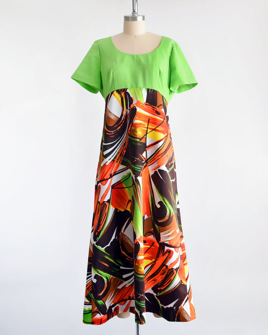 A vintage 70s maxi dress with a lime green bodice with short sleeves and a maxi skirt that is white with an abstract browns, oranges, greens, and yellow large brushstroke print. The dress is on a dress form.