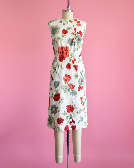 A vintage 60s white dress with a large red and green floral print on a dress form.